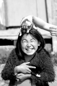 Une fillette inuite se fait faire un massage par un chiot (de chien de traîneau). Elle représente la future génération de femmes groenlandaises